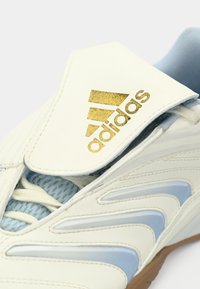 Krupan plan bijele Adidas sportske tenisice sa zlatnim logotipom na jeziku i svijetloplavim naglascima sa strane i unutarnjom postavom.