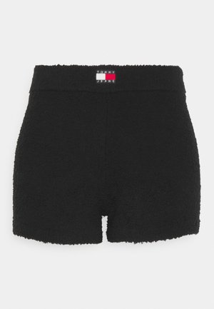 Czarne, pluszowe szorty o wysokim stanie z naszywką z logo Tommy Jeans na pasku, płaskim przodem i małym centralnym rozcięciem u dołu.