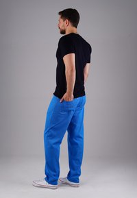 Dunkles kurzärmliges T-Shirt kombiniert mit lässigen blauen Hosen; verfügt über Taschen und einen strukturierten Stoff. Weiße Sneakers runden den Look ab.