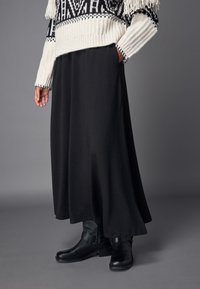 Jupe maxi noire en tissu texturé, associée à un pull en tricot à motifs blancs et noirs et à des bottines noires. 