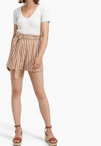 Top blanco de manga corta con textura acanalada combinado con pantalones cortos de talle alto a rayas marrones y blancas, con cinturón atado. Sandalias de cuña color beige.