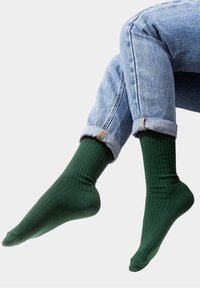 Zielone skarpetki w prążki wykonane z mieszanki bawełny, z dopasowanym kształtem i klasycznym ściągaczem, połączone z podwiniętymi jasnoniebieskimi dżinsami.