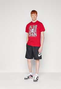 Red short-sleeve t-shirt with a graphic print featuring "AIR JORDAN," paired with black shorts and black-and-white low-top sneakers.