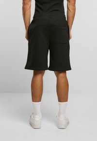 Svart bomull idrettsshorts med avslappet passform, kne-lengde, med en enkelt baklomme og rullede sømmer, sammen med hvite joggesko.