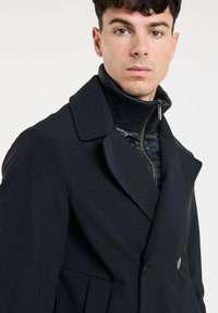Marine peacoat met een dubbelzijdig ontwerp, grote revers en een hoge kraag. Bevat een binnenjack met rits van een gestructureerde stof.
