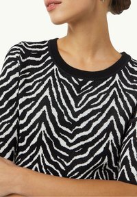 Maglione a righe zebra bianco e nero in maglia, con scollo rotondo, maniche corte e una finitura testurizzata. Accentuato da un colletto nero solido.