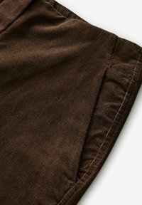 Brun kordfløjlstof med en subtil ribbet tekstur. Billedet viser en del af et beklædningsstykke med en ren kant og ingen synlige beslag.