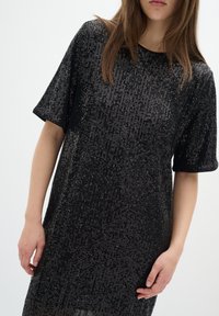 Svart paljettklänning med korta ärmar, rund halsringning och vertikal paljettstruktur som skapar en glittrande effekt genom hela klänningen.