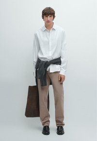 Weiß gestreifte, kurzärmelige Hemd mit vertikalen Streifen, grauer Pullover um die Taille gebunden, khakifarbene Hose, schwarze Schuhe, braune Tragetasche. Einfaches Design und Farben.