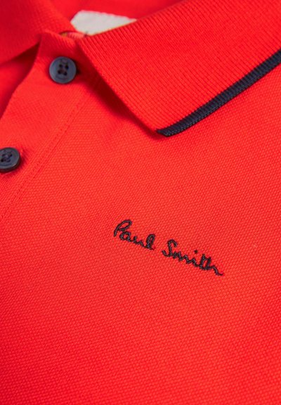 Sarkana polo krekls, izgatavots no teksturēta auduma, ar melnu apkakli, divām melnām pogām un izšūtu "Paul Smith" logo melnā krāsā.