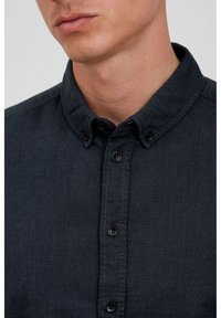 Camisa de botones de color gris oscuro con cuello, con botones negros y tejido texturizado. No se observan patrones ni detalles destacados.