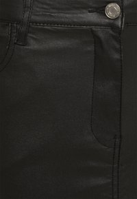 Svarta syntetiska leggings med en slät textur, prydda med en silverfärgad metallknapp och standard fickdesign på framsidan.