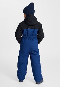 Peto de nieve azul infantil con sección superior negra, cintura elástica y capucha. Presenta una franja reflectante blanca en la parte trasera.