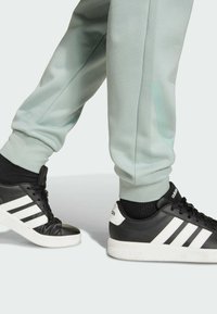 Black and white sneakers with textured leather and a white rubber sole, paired with mint green joggers featuring a slight sheen and tapered cuffs.