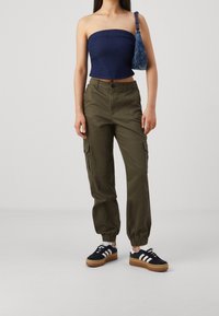 Džínový top bez ramínek, olivově zelené cargo kalhoty s bočními kapsami a černé tenisky s bíl�ými pruhy a robustní podrážkou.