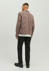 Giubbino di denim marrone con taglio dritto, dettagli con bottoni e due tasche laterali, abbinato a pantaloni neri e stivali alla caviglia.