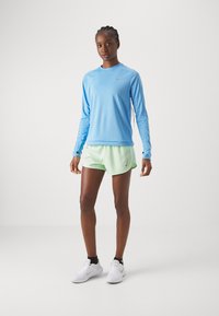 Lyseblå langermet treningstopp med rund hals og grå Nike-logo, kombinert med myntegrønne shorts og hvite joggesko. Glatt stofffinish.