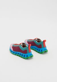 Ténis coloridos com uma parte superior em malha nas cores vinho, azul-piscina e rosa, com uma sola robusta em azul e verde. Inclui detalhes em vermelho e um design com atacadores.