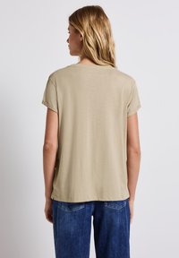 Camiseta de manga corta color caqui con un corte holgado, escote redondo y una textura suave, combinada con vaqueros de mezclilla azules que cuentan con bolsillos traseros.