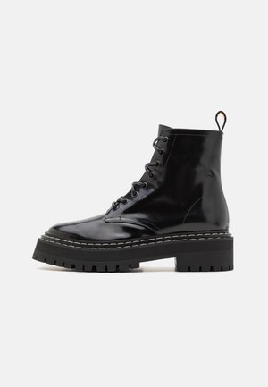 Botines negros brillantes a la altura del tobillo con un diseño de cordones, que cuentan con una suela texturizada gruesa y costuras en contraste a lo largo del borde. Resistentes y duraderos.