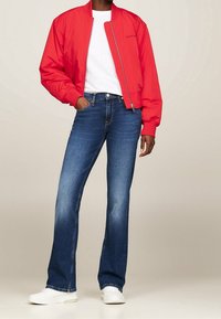Chaqueta bomber roja con cremallera al frente, camiseta de cuello redondo blanca, vaqueros acampanados oscuros y zapatillas blancas, enfatizando un estilo de atuendo casual.