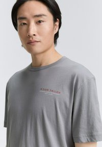 Grå bomulds t-shirt med korte ærmer og rund halsudskæring, prydet med et lille rødt "TOM TAILOR" logo på brystet.