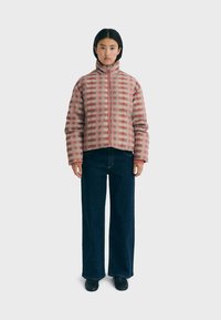 Checkered puffer jacket in shades of pink and red, zip front, high collar, quilted texture. Paired with loose dark blue jeans and black footwear.