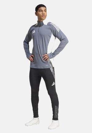 Grijze sporttop met lange mouwen, hoge kraag en een kwart rits, gecombineerd met zwarte leggings met een gekleed zijaccent en witte logo's.