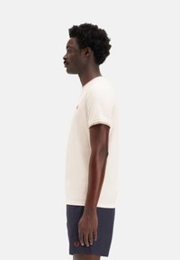 Camiseta de manga corta color crema con cuello acanalado en contraste y logo bordado en el pecho, combinada con pantalones cortos de color marino. Diseño sencillo, ajuste casual.