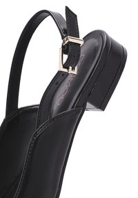 Sandal in pelle nera con punta chiusa e cinturino regolabile con fibbia, dotato di tacco sagomato e superficie interna liscia.
