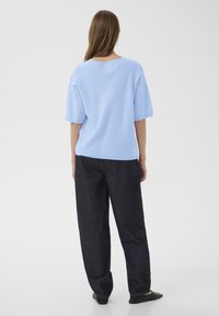 Hele sinine lühikeste varrukatega kootud pluus ümmarguse kaelusega, kombineeritud tumedate denimist laiade pükstega ja mustade tasaste kingadega. Pehme tekstuur, lõdvestunud istuvus.