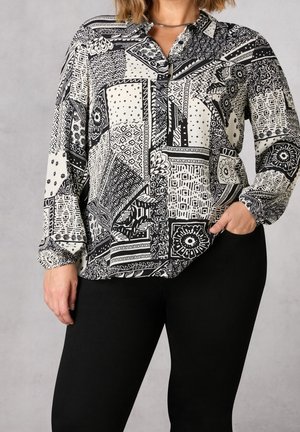 Langsleeve blouse in zwart-wit met een kraag, met verschillende geometrische ontwerpen en een relaxte pasvorm. Zwarte broek eronder gedragen.