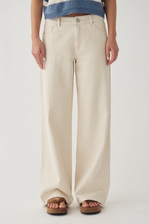 Wijde crèmekleurige broek gedragen met bruine platformsandalen en een cropped blauwe gebreide trui, staand tegen een effen achtergrond.