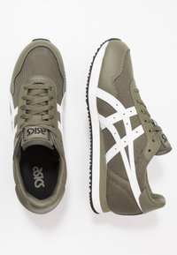 Zielone sportowe buty z siateczką i skórą, z białymi paskami i sznurówkami; zaokrąglony nosek, teksturowany wierzch i czarne wnętrze.