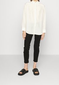 Wit, lange mouwen button-up shirt gecombineerd met zwarte slim-fit broek en zwarte slippers, met een gladde stof en minimalistisch ontwerp.