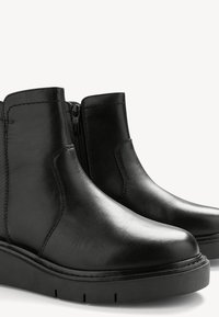 Schwarze Leder-Stiefeletten mit einer glatten Textur, runder Zehenpartie, seitlichem Reißverschluss und einer dicken schwarzen Gummisohle mit Rillen.