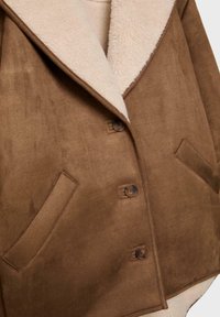 Hnedý semišový kabát s béžovým fleece podšívkou, tromi gombíkmi a dvoma šikmými prednými vreckami.