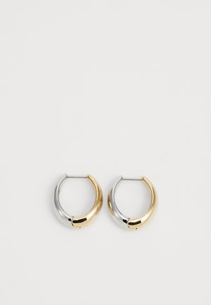 Para małych kolczyków koła, wykonanych w połowie ze złota, a w połowie ze srebra, o gładkim, zaokrąglonym wzorze, prezentowana na jasnym tle.