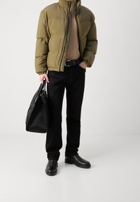 Giacca a vento verde oliva con collo rialzato, maglione beige, pantaloni neri a sigaretta e stivali in pelle nera. Borsa a tracolla nera con texture.