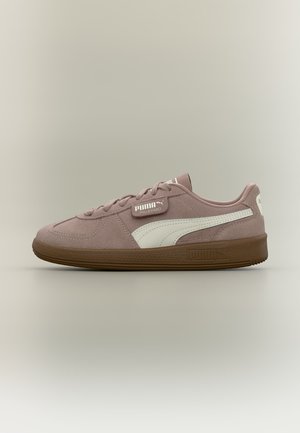 Niskie sneakersy Puma Palermo w pudrowo-różowym zamszu z białym paskiem bocznym i brązową gumową podeszwą, widoczne z zewnętrznej strony.
