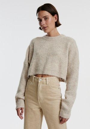 Beige cropped sweater with a ribbed texture and long sleeves, paired with high-waisted khaki pants featuring a button closure and pockets.