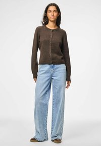 Cardigan marrone con bottoni, dal collo rotondo, abbinato a jeans a gamba larga blu chiaro e scarpe marroni; texture a maglia liscia.