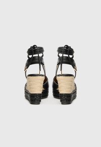 Schwarze Leder-ESPADRILLES mit einem gewebten Jute-Absatz, ausgestattet mit einer geflochtenen schwarzen Basis und überkreuzten Knöchelriemen für zusätzlichen Halt.