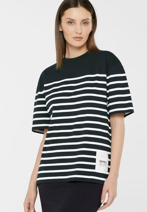 Woman with straight brown hair wearing a black and white horizontal striped short-sleeve shirt with a white label near the hem.