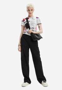 Biała graficzna koszulka z napisem i kolorowymi akcentami, w połączeniu z czarnymi spodniami cargo. Czarna torba na ramię i białe trampki dopełniają look.