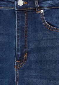Tela de denim con costuras naranjas, mostrando la sección del bolsillo delantero, el lazo del cinturón y el botón de metal en unos jeans azules.