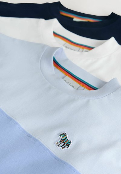 Drei Baumwoll-T-Shirts in Hellblau, Weiß und Marineblau. Jedes hat einen Rundhalsausschnitt und ein kleines, aufgesticktes Zebramotiv auf der Vorderseite.