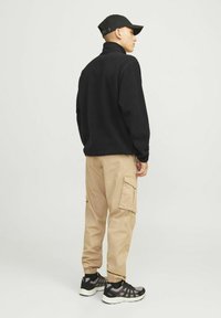 Black fleece jacket with high collar, beige cargo pants with side pockets, and black athletic shoes on a neutral background.
