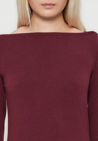 Bordeaux, lange mouw top met een off-the-shoulder halslijn. Gemaakt van een zachte, elastische stof met een gladde textuur.