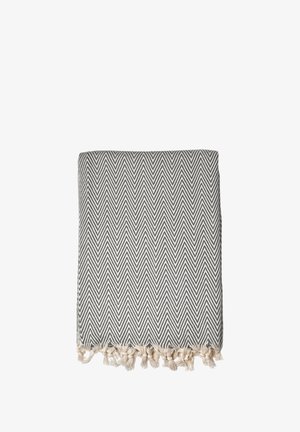 Manta tejida con un patrón de espiga en gris y blanco, con bordes flecados en beige. Textura suave, forma rectangular.